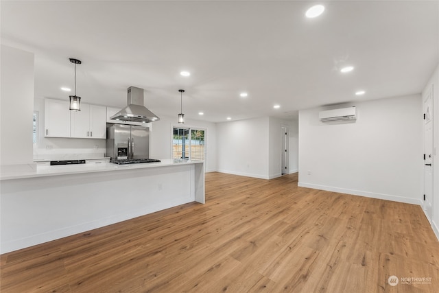 kitchen featuring stainless steel appliances, light hardwood / wood-style floors, pendant lighting, wall chimney range hood, and white cabinetry