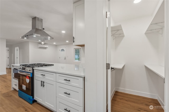 kitchen featuring light hardwood / wood-style floors, a wall mounted air conditioner, gas stove, white cabinets, and island exhaust hood