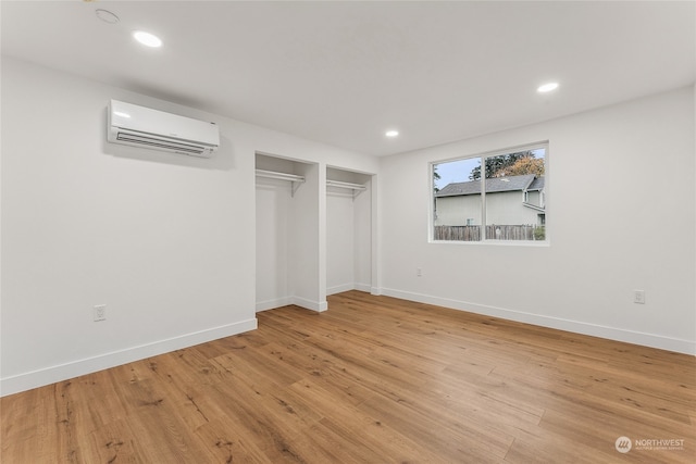 unfurnished bedroom featuring light hardwood / wood-style floors and an AC wall unit