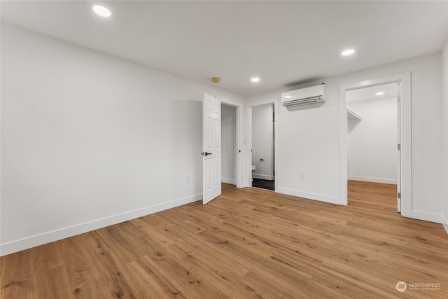 unfurnished bedroom with a wall mounted AC, light hardwood / wood-style flooring, and a spacious closet