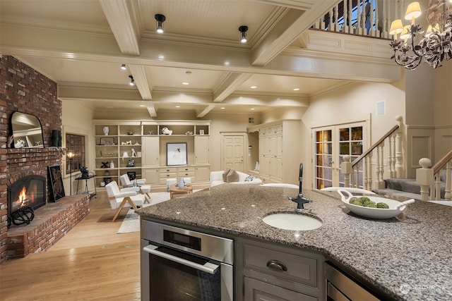 kitchen with a brick fireplace, sink, dark stone countertops, beamed ceiling, and light hardwood / wood-style floors