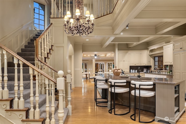 kitchen with light wood-type flooring, beam ceiling, dark stone countertops, white cabinets, and hanging light fixtures