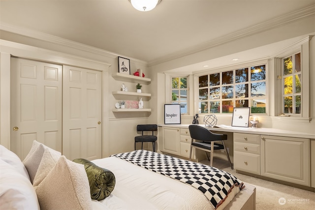 bedroom featuring built in desk, crown molding, light carpet, and a closet