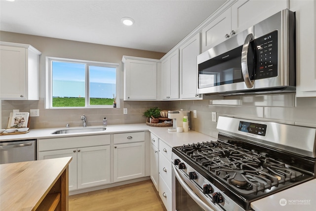 kitchen with appliances with stainless steel finishes, sink, white cabinets, backsplash, and light wood-type flooring