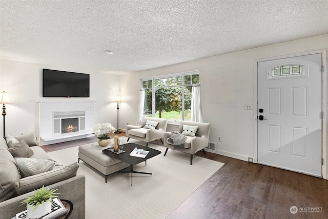 living room with wood-type flooring, a textured ceiling, and a brick fireplace