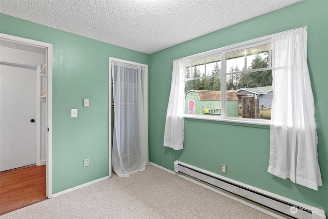 unfurnished bedroom with a textured ceiling, baseboard heating, and light carpet