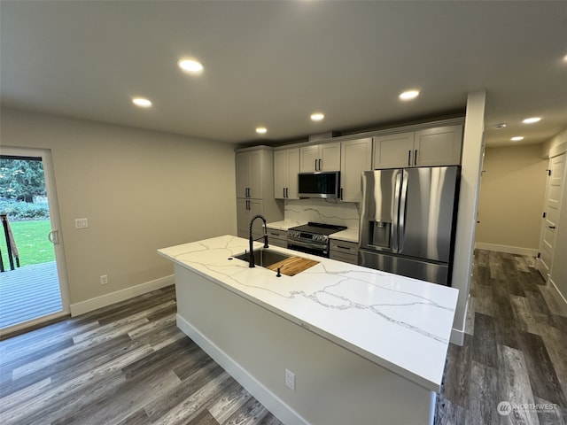 kitchen with a center island with sink, appliances with stainless steel finishes, light stone counters, and gray cabinetry