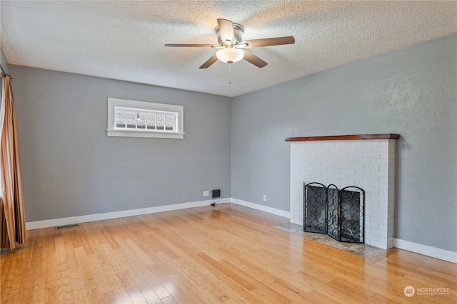 unfurnished living room with a textured ceiling, ceiling fan, light hardwood / wood-style flooring, and a brick fireplace