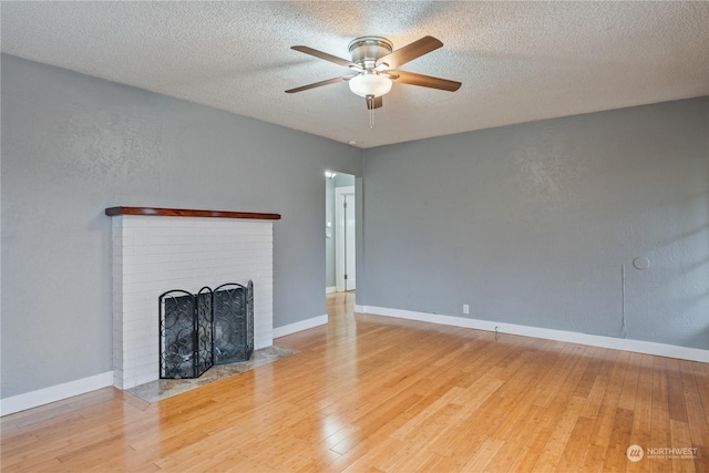 unfurnished living room with ceiling fan, a fireplace, a textured ceiling, and light wood-type flooring