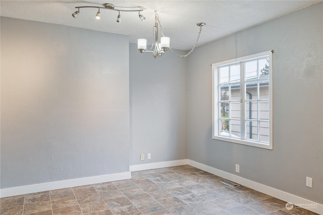 empty room with plenty of natural light, a textured ceiling, and a chandelier