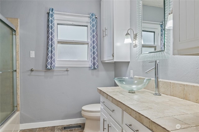 full bathroom with combined bath / shower with glass door, vanity, toilet, and plenty of natural light