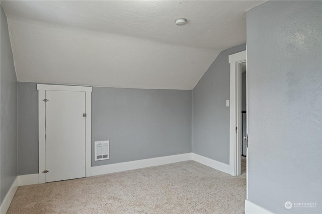 additional living space featuring light carpet, a textured ceiling, heating unit, and vaulted ceiling