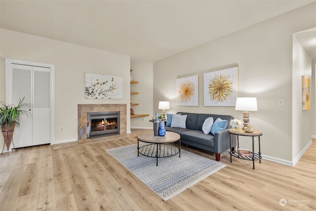 living room featuring light wood-type flooring, a fireplace, and built in features