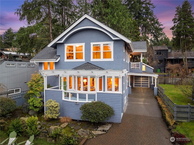 back house at dusk featuring a garage and a balcony