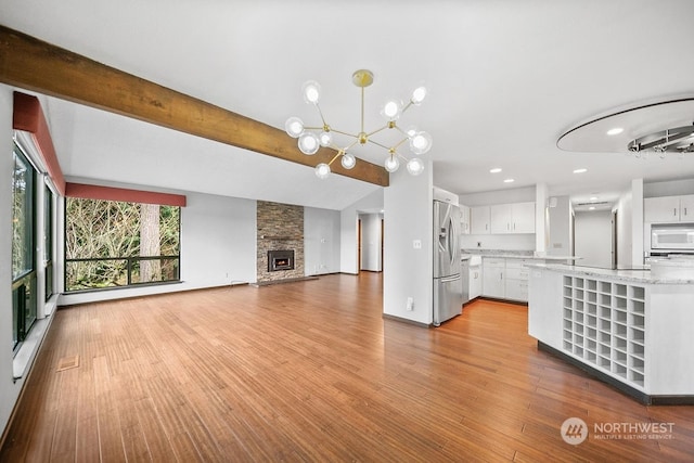 kitchen with stainless steel fridge, light wood-type flooring, a fireplace, a chandelier, and white cabinetry