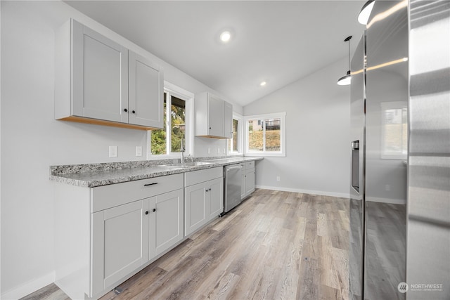 kitchen with light stone counters, stainless steel appliances, white cabinets, lofted ceiling, and light hardwood / wood-style flooring