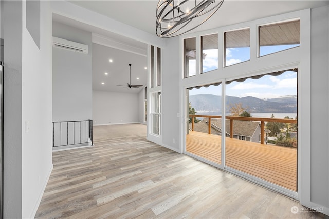 spare room featuring a mountain view, light wood-type flooring, ceiling fan with notable chandelier, and a wall mounted AC