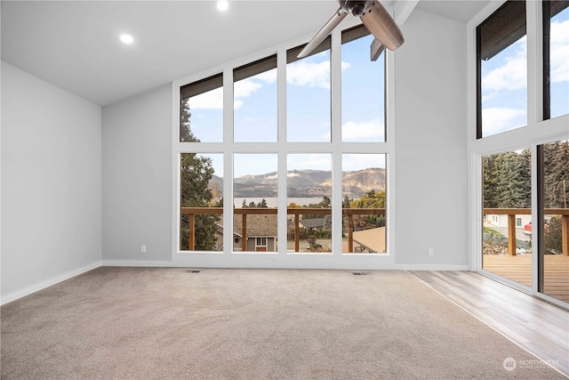 spare room with hardwood / wood-style floors, a wealth of natural light, a mountain view, and high vaulted ceiling