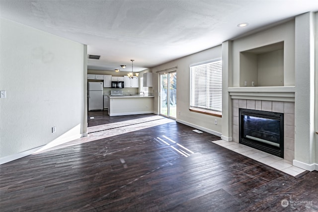 unfurnished living room featuring a chandelier, a tile fireplace, light wood-type flooring, and a textured ceiling