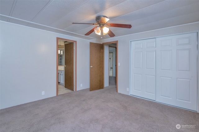 unfurnished bedroom featuring light colored carpet, a textured ceiling, connected bathroom, ceiling fan, and a closet