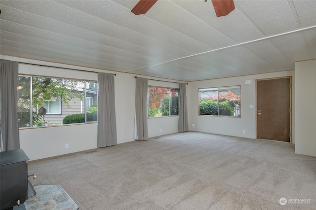 carpeted empty room with a wood stove and ceiling fan