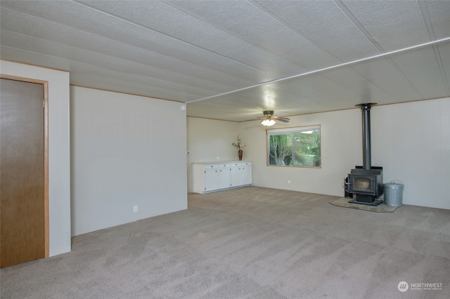 unfurnished living room featuring a wood stove, light colored carpet, and ceiling fan