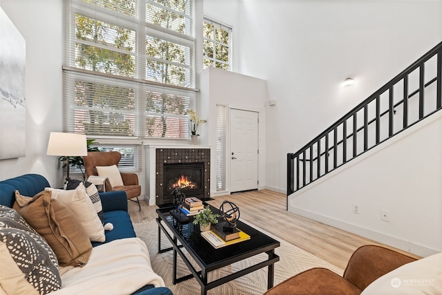 living room with light wood-type flooring, a fireplace, and a towering ceiling