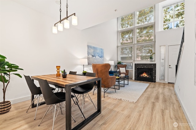 dining space with a tile fireplace, a high ceiling, light wood-type flooring, and a wealth of natural light