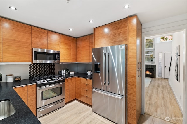 kitchen featuring sink, decorative backsplash, a fireplace, light hardwood / wood-style floors, and stainless steel appliances