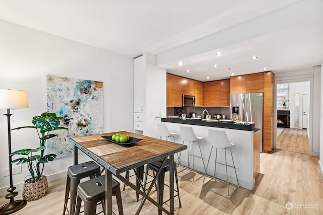 kitchen with sink, a kitchen breakfast bar, decorative backsplash, appliances with stainless steel finishes, and light wood-type flooring