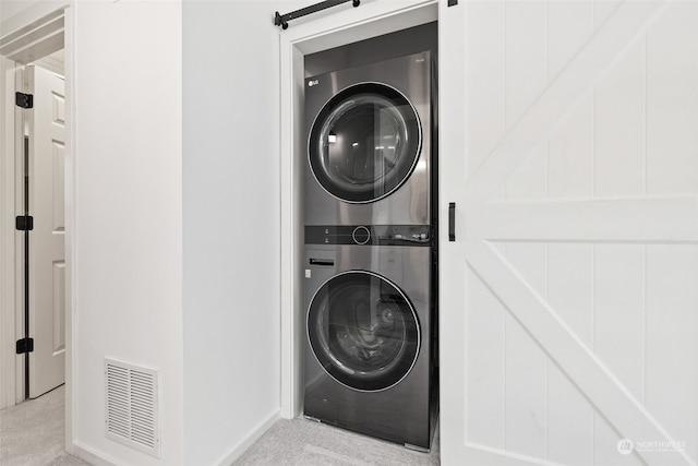 laundry area with a barn door, light colored carpet, and stacked washer and clothes dryer