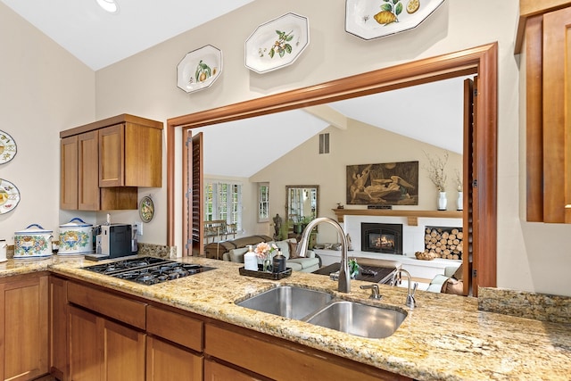 kitchen featuring sink, vaulted ceiling with beams, light stone counters, kitchen peninsula, and stainless steel gas stovetop