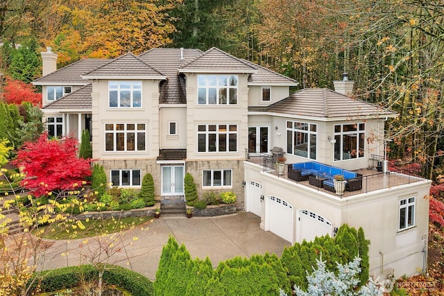 view of front of home with a chimney, stucco siding, a balcony, a garage, and stone siding