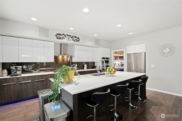 kitchen with dark brown cabinets, high end fridge, a kitchen breakfast bar, dark wood-type flooring, and a kitchen island with sink