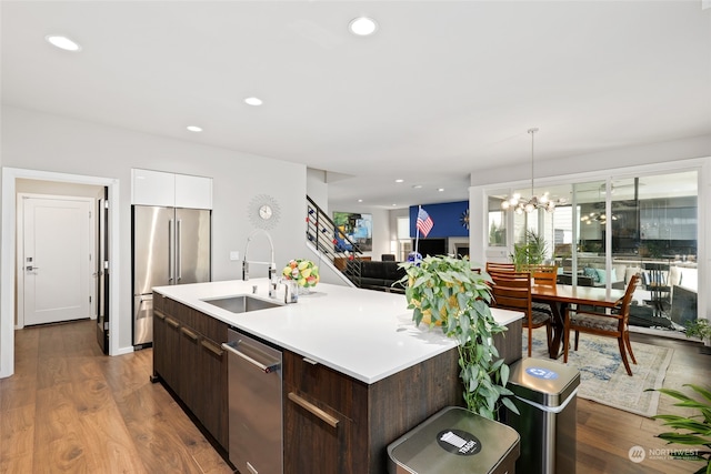 kitchen featuring hardwood / wood-style floors, dark brown cabinetry, sink, a kitchen island with sink, and appliances with stainless steel finishes