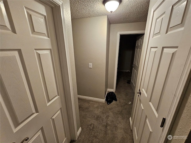 hallway with dark colored carpet and a textured ceiling