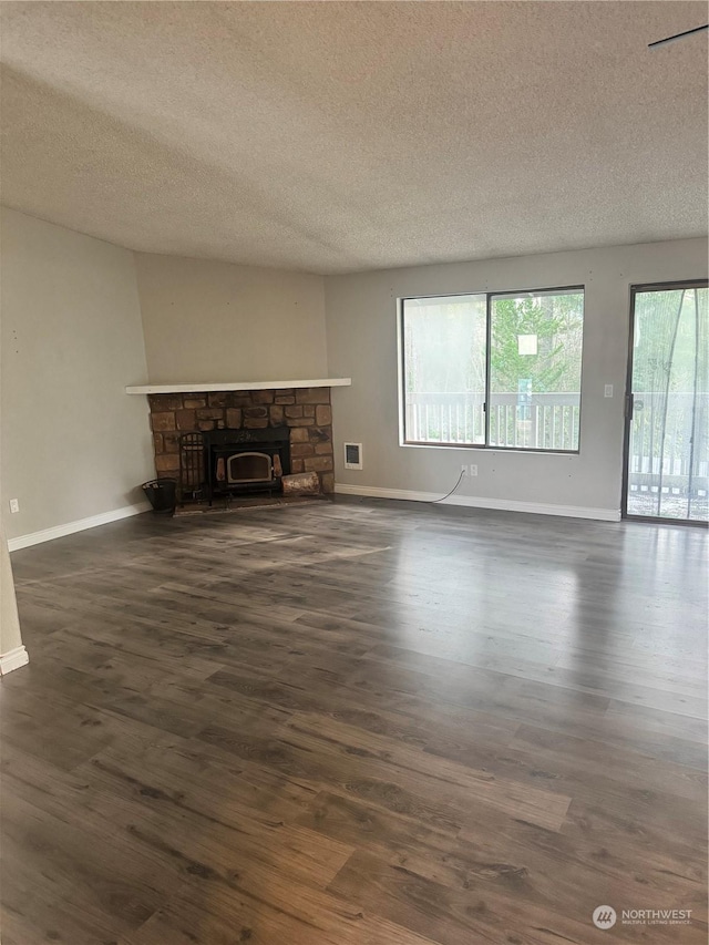 unfurnished living room featuring dark hardwood / wood-style floors, a stone fireplace, and a textured ceiling