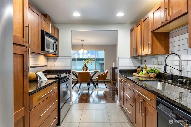 kitchen featuring sink, dark stone counters, pendant lighting, appliances with stainless steel finishes, and light wood-type flooring