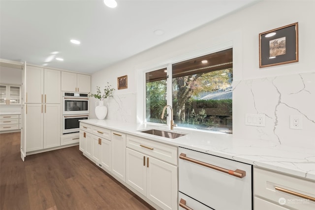 kitchen with light stone countertops, white appliances, white cabinetry, and a sink