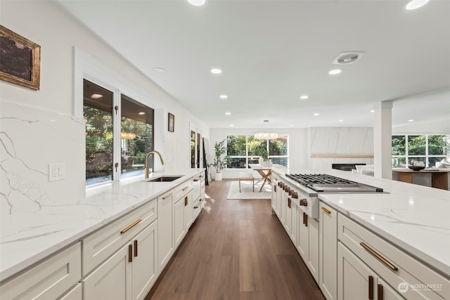 kitchen with light stone counters, dark wood-type flooring, white cabinetry, stainless steel gas cooktop, and a sink