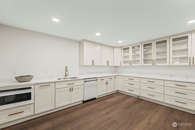 kitchen featuring dishwasher, light stone counters, glass insert cabinets, dark wood-type flooring, and a sink