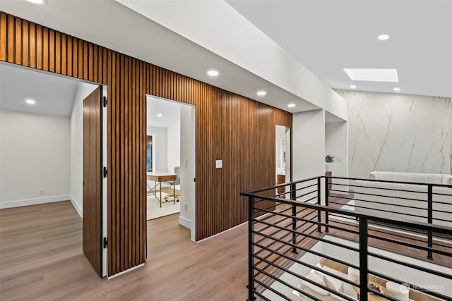 hallway featuring a skylight, baseboards, an upstairs landing, light wood-type flooring, and recessed lighting