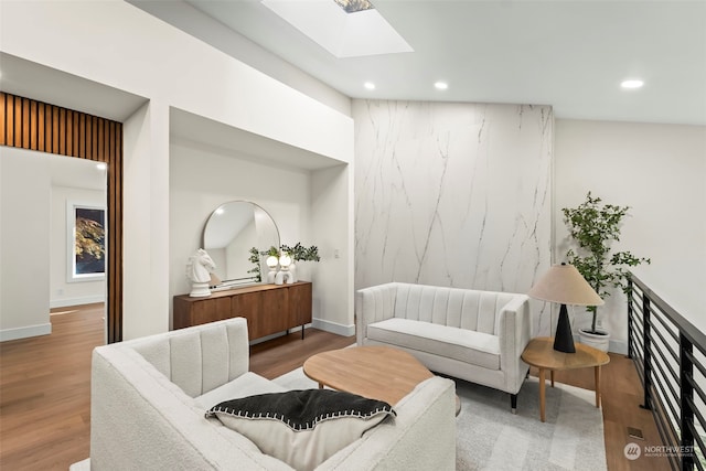 living area featuring a skylight, an accent wall, wood finished floors, and recessed lighting