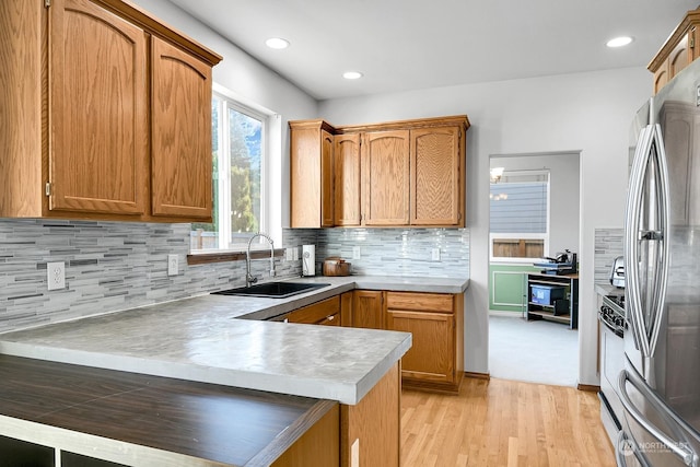 kitchen featuring kitchen peninsula, stainless steel fridge, backsplash, sink, and light hardwood / wood-style flooring