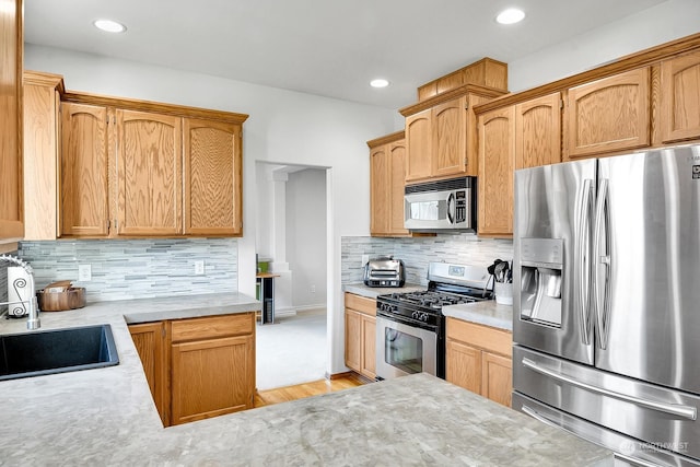 kitchen with tasteful backsplash, sink, stainless steel appliances, and light hardwood / wood-style flooring