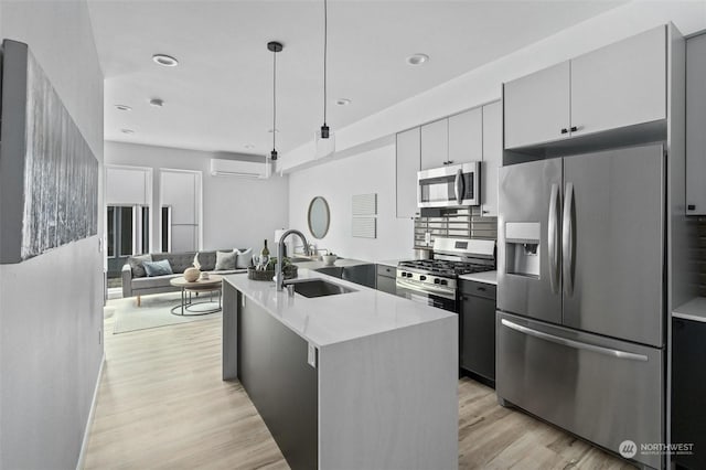 kitchen with sink, light hardwood / wood-style floors, decorative light fixtures, a center island with sink, and appliances with stainless steel finishes