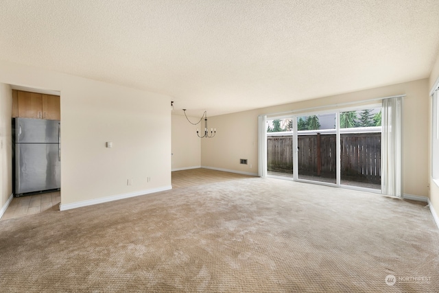 carpeted empty room with a textured ceiling and a chandelier