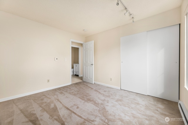 unfurnished bedroom with baseboard heating, light carpet, a closet, and rail lighting