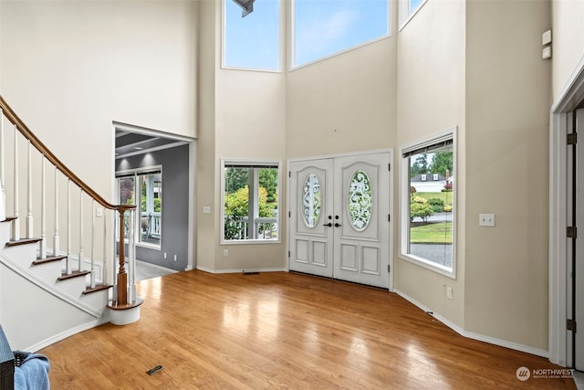 entryway with light hardwood / wood-style floors, french doors, a healthy amount of sunlight, and a towering ceiling