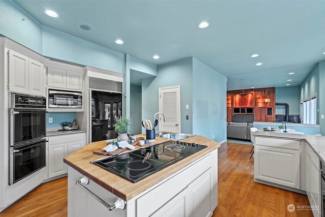 kitchen featuring white cabinets, black appliances, a kitchen island, and light wood-type flooring